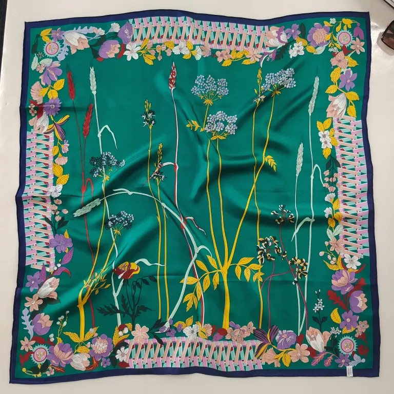 A premium green mulberry silk square scarf featuring detailed illustrations of wild plants, flowers, and wheat stalks in the center, surrounded by a vintage pastoral border with pink fences and colorful blossoms, finished with a dark blue hem.