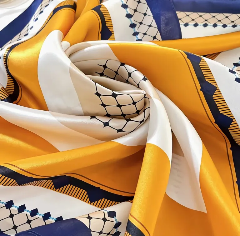 A luxury 100% mulberry silk square scarf measuring 68x68cm, elegantly swirled to display its premium satin texture, vibrant mustard yellow, navy blue, and white geometric patterns.