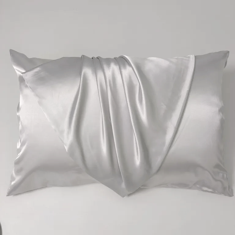 A pearl white mulberry silk pillowcase with luxurious fluid satin folds and elegant drapes on a clean light gray background.