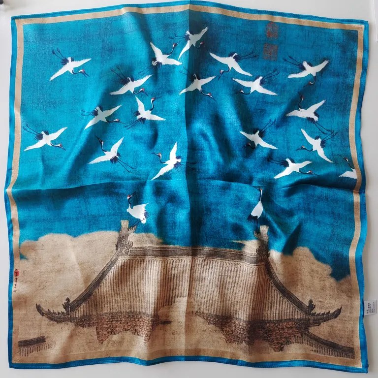 Flat lay view of a Docsun 68cm mulberry silk square scarf featuring a vintage oriental flying crane and ancient palace roof pattern with a champagne gold border.