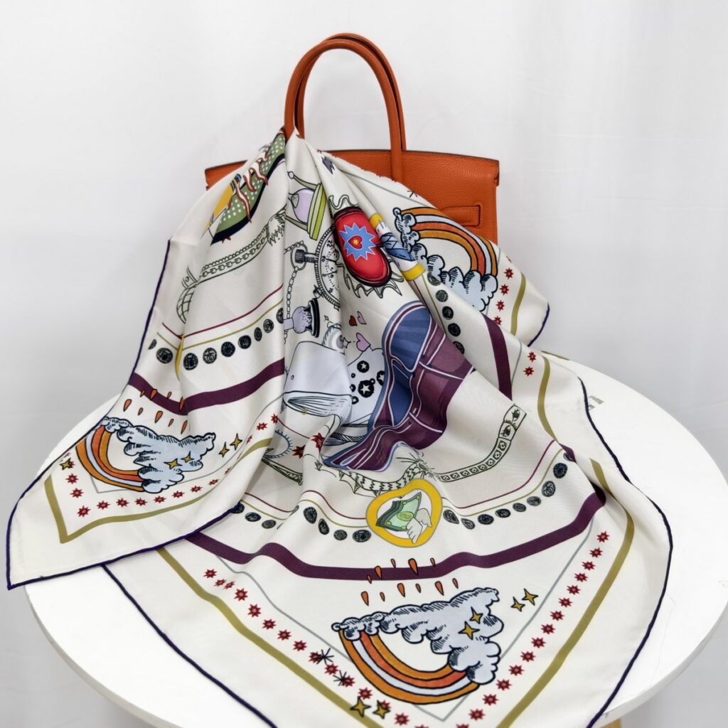 A DOCSUN 90cm mulberry silk square scarf with an artistic unicorn, rainbow, and star illustration, elegantly draped over an orange leather handbag.