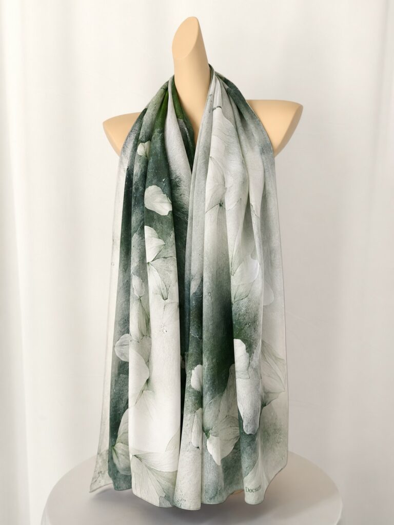 100% mulberry silk scarf draped on a mannequin, featuring white floral prints and soft green botanical tones.