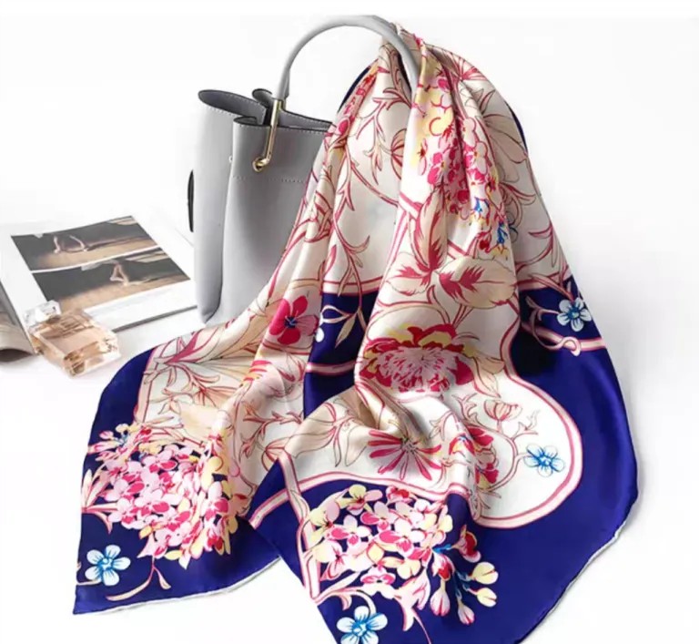 Blue and white floral silk scarf styled with a grey handbag, featuring pink floral branches and a deep blue border.