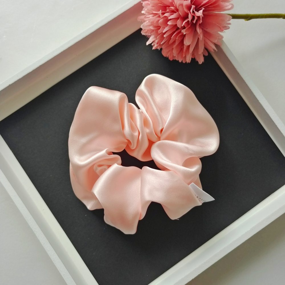 Light pink silk scrunchie with smooth shine and large soft folds for elegant hair styling.