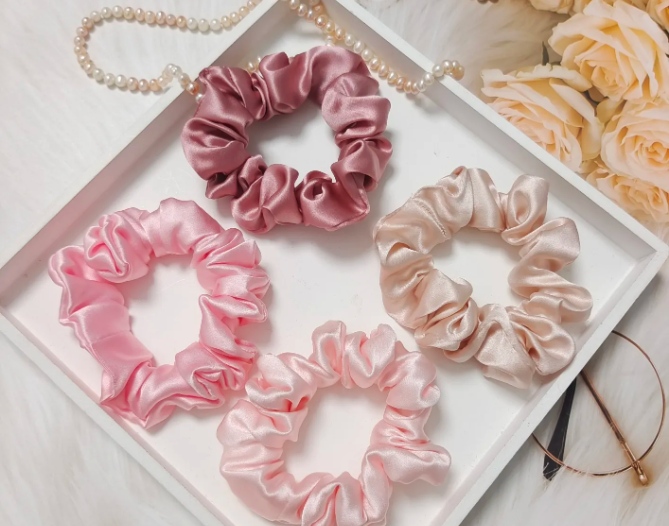 Pink silk scrunchie set displayed on a white tray with pearl necklace and rose decorations.