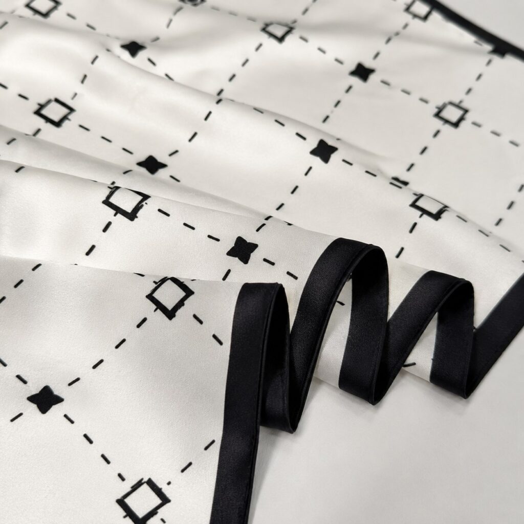 A close-up view showing the silk sheen, black edge finish, and minimalist geometric print.